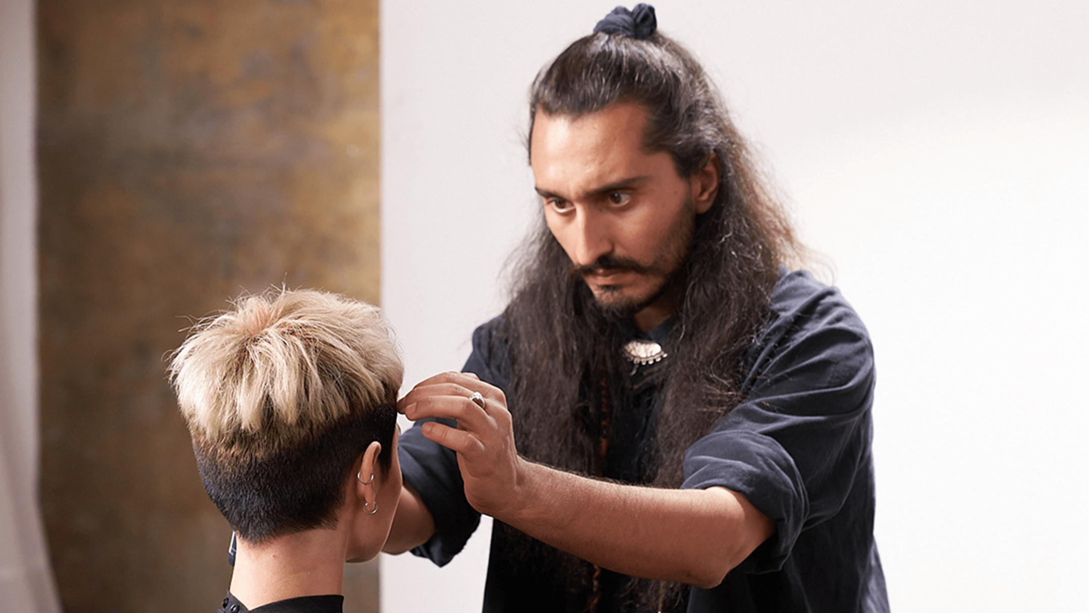 Barber with long hair and black shirt styling hair