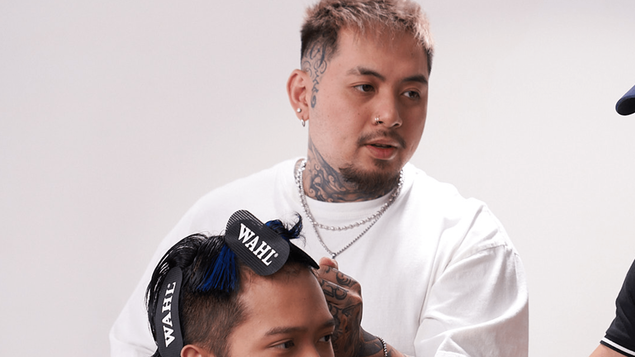 Barber with face tattoos and goatee wearing a white shirt styling hair